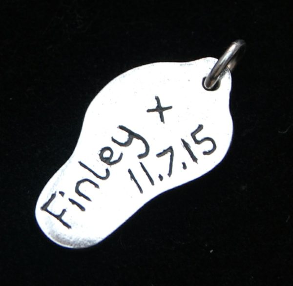 Silver charm cut out in the shape of the footprint. Name and date hand inscribed on the back.