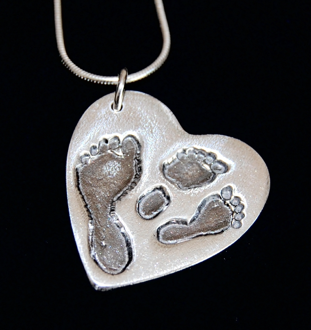 Large silver heart charm with footprints from a set of twins and their older sibling. Names are hand inscribed on the back.