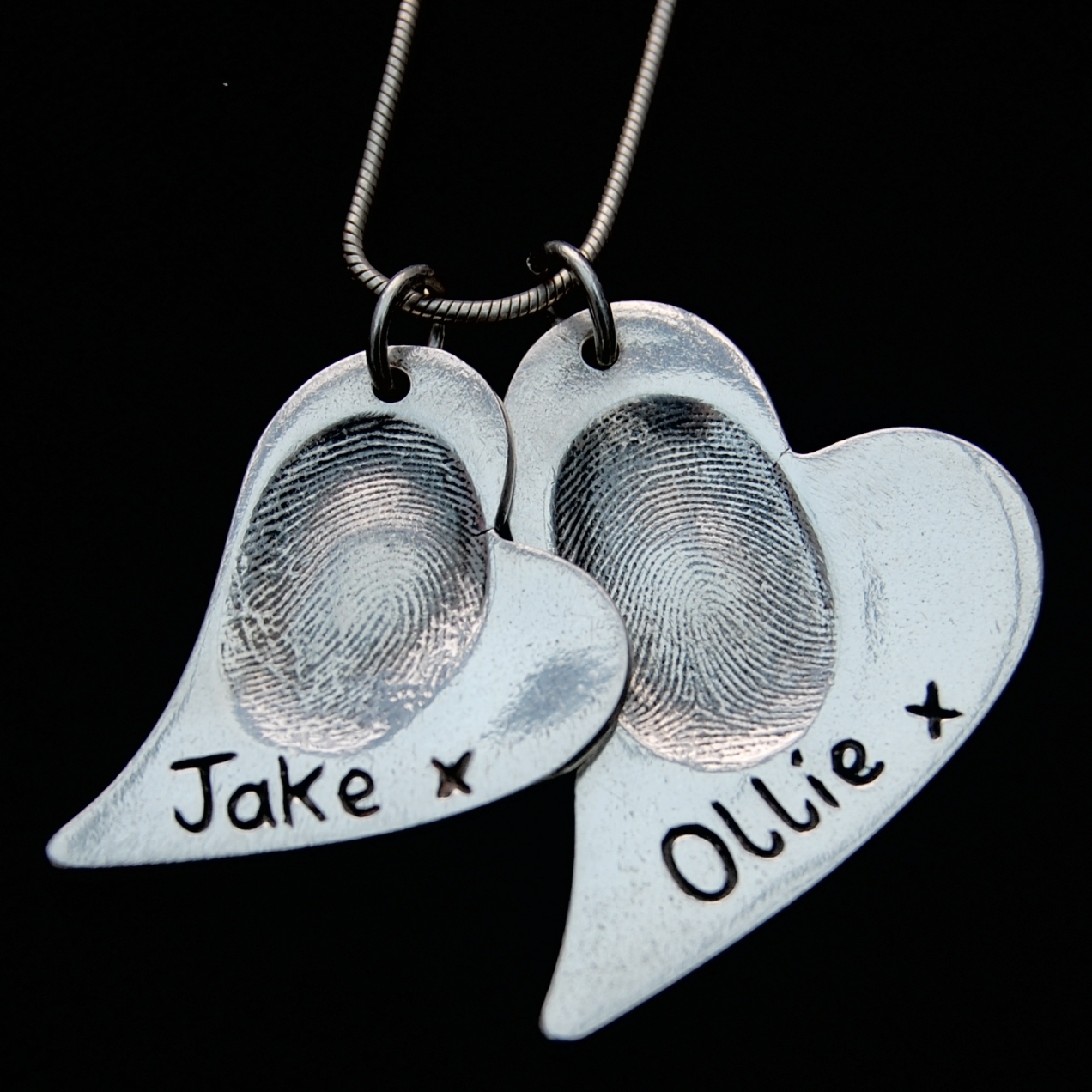 Regular and large curved heart silver fingerprint charms on a chain. These charms have names hand inscribed on the front alongside the fingerprints.
