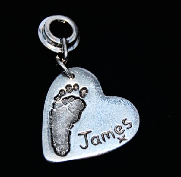 Regular silver heart footprint charm presented on a charm carrier ready to add to a bracelet or necklace.