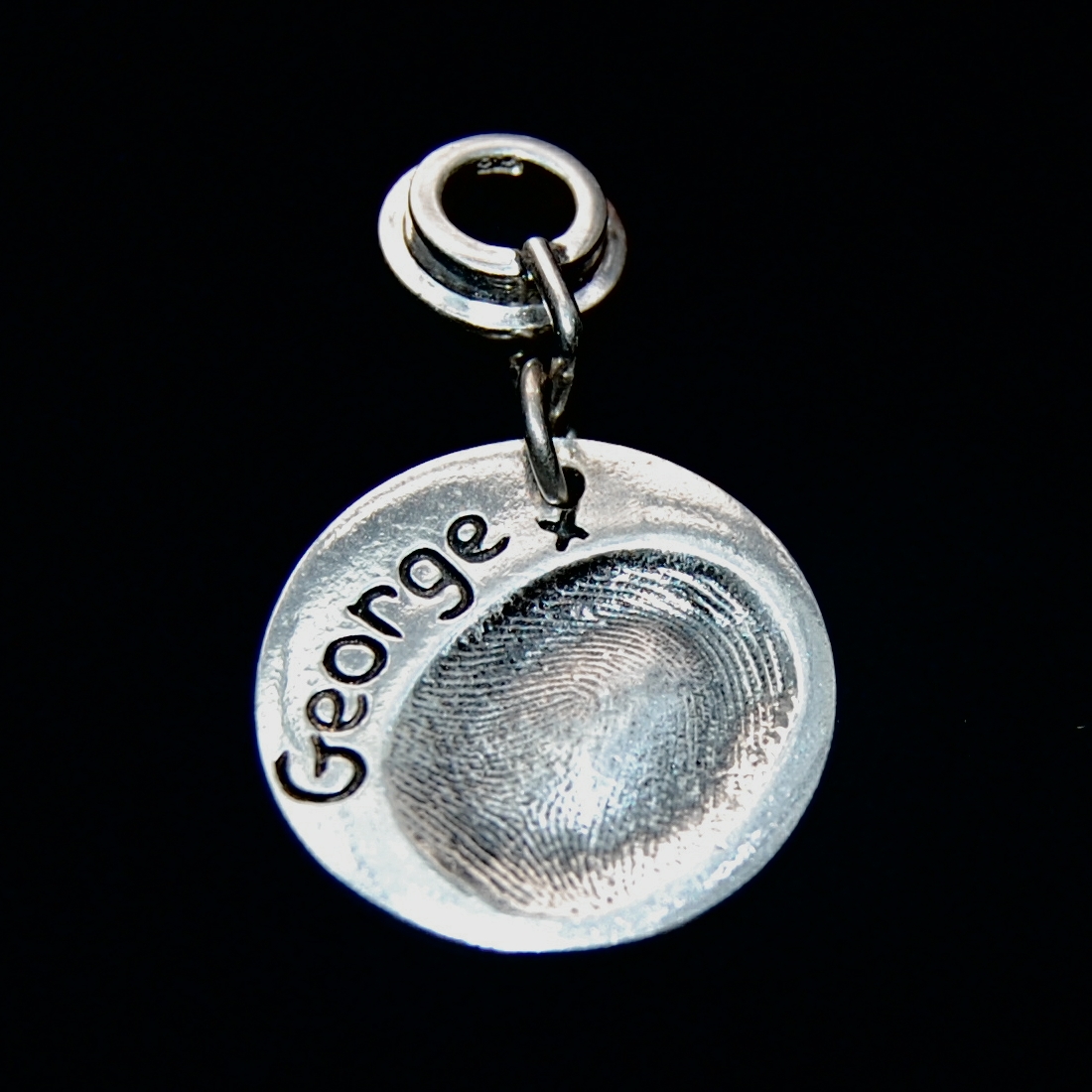 Regular circle shaped silver fingerprint charm presented on a charm carrier.