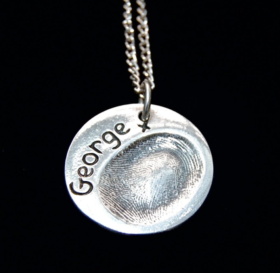 Regular circle shaped silver fingerprint charm with name hand inscribed on the front.