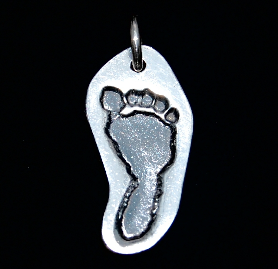 Small silver footprint charm cut out in the shape of the footprint. Name hand inscribed on the back.
