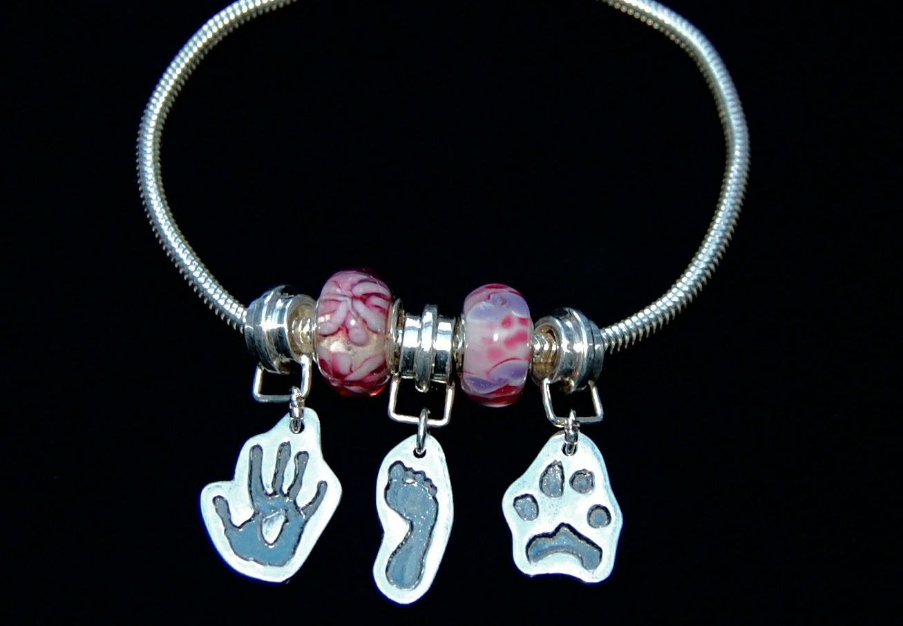 Pandora style bracelet with cut out hand, foot and paw print charms. Names hand inscribed on the backs of the charms.