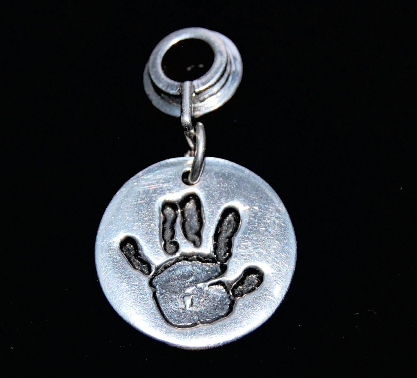 Small silver circle handprint charm presented on a charm carrier. Name is hand inscribed on the back.