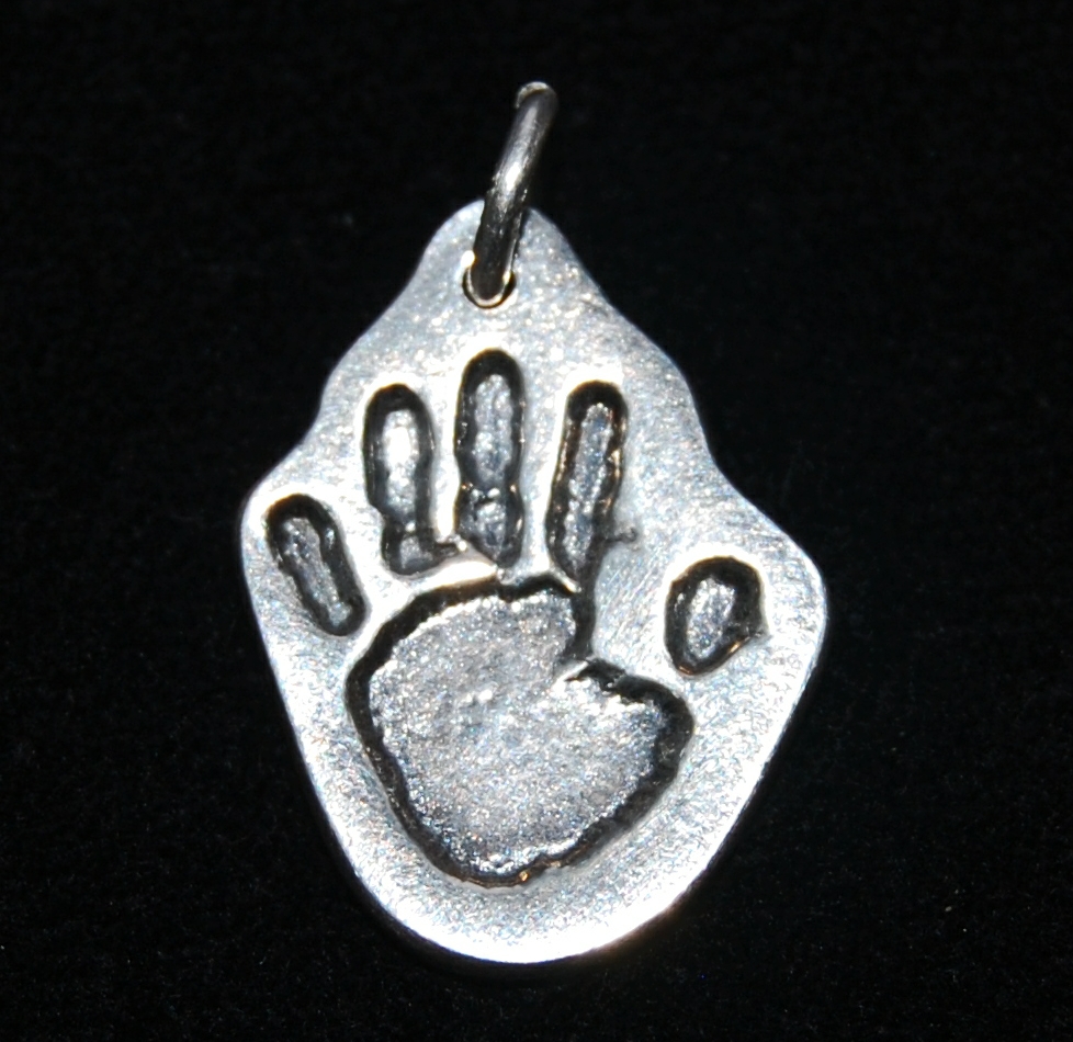 Small silver charm cut by hand in the shape of the handprint. Name hand inscribed on the back.