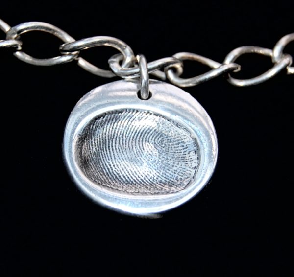 Small circle shaped silver fingerprint charm with name hand inscribed on the reverse.