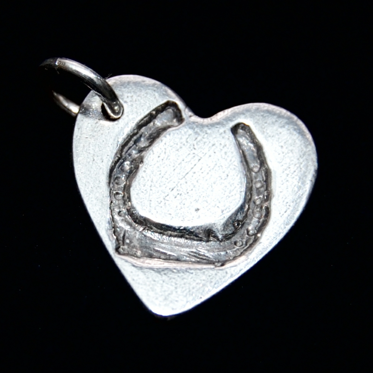 Small silver heart charm with horse shoe imprint on the front and name hand inscribed on the back.